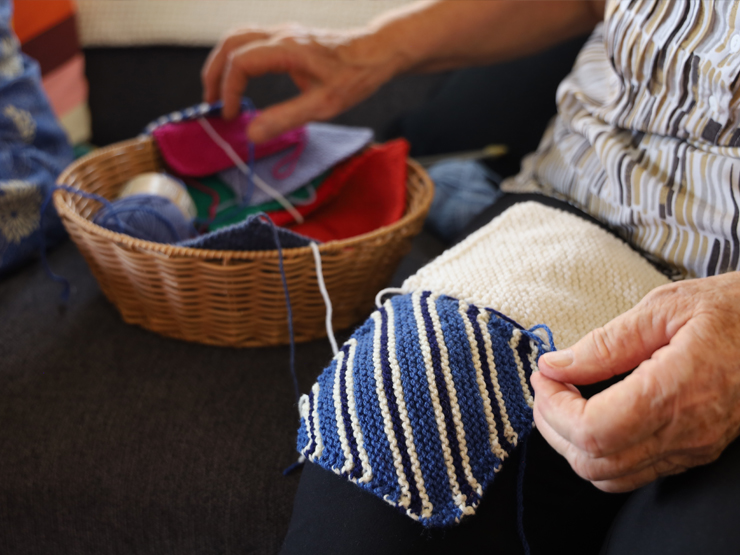 An older person knitting a square patch for a blanket.