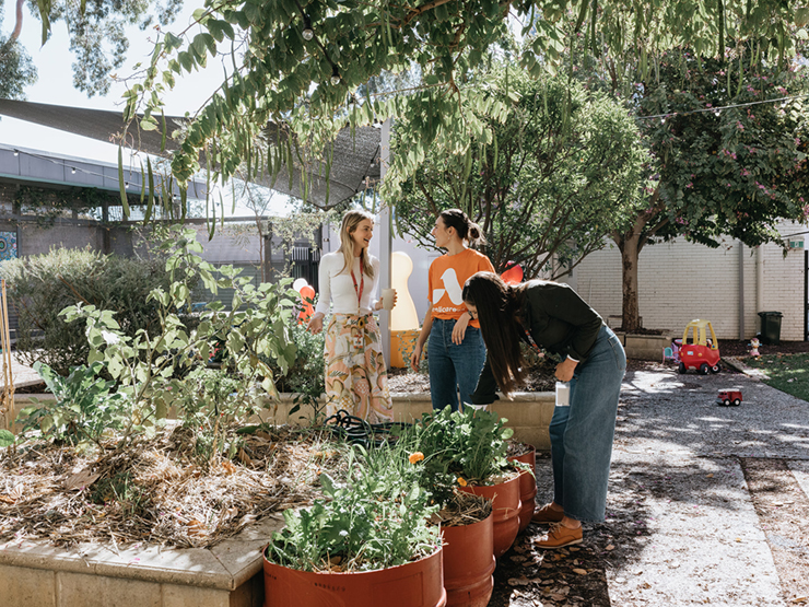 Three Anglicare WA workers standing in a garden next to a raised garden bed with vegetables in it.