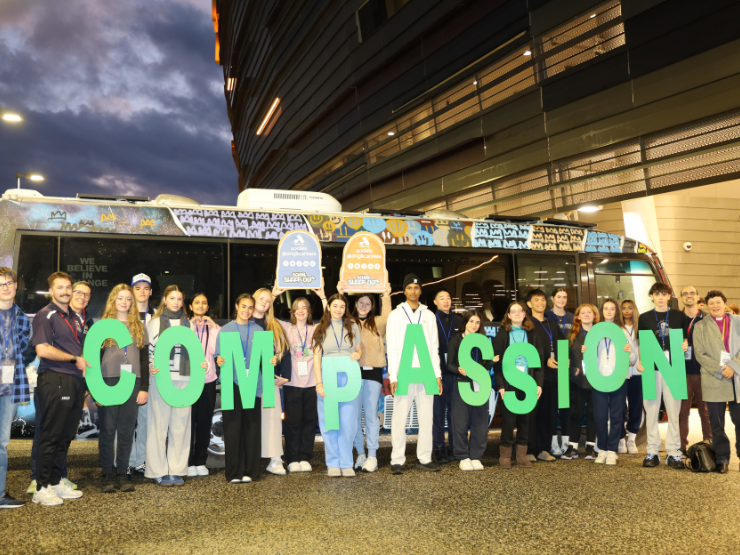 A group of teenagers standing in front of the Street Connect Bus holding letters that spell out the word compassion.